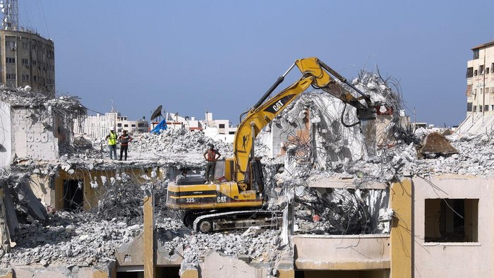 Palestinian workers use a backhoe to break and remove parts of the Al-Jawhara building, that was damaged in Israeli airstrikes during Israel's war with Gaza's Hamas rulers last May, in the central al-Rimal neighborhood of Gaza City, Nov. 16, 2021. The Gaza Strip has few jobs, little electricity and almost no natural resources. But after four bruising wars with Israel in just over a decade, it has lots of rubble. Local businesses are now finding ways to cash in on the chunks of smashed concrete, bricks and debris left behind by years of conflict. (AP Photo/Adel Hana)