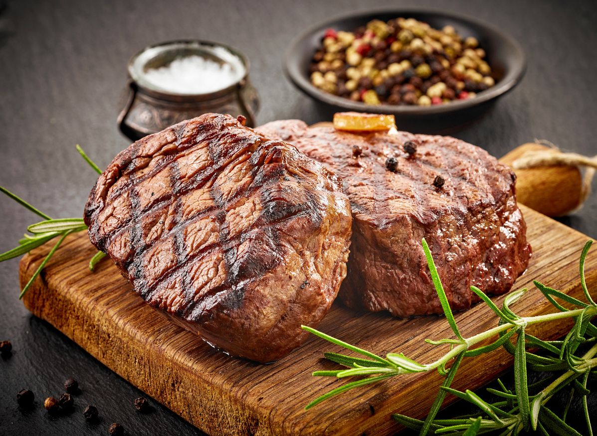 grilled beef steaks with spices on wooden cutting board
