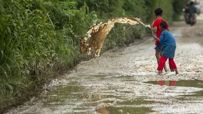 Dua anak menguras jalan berlubang yang tegenang di Jalan Raya Kali CBL, Cibitung, Kabupaten Bekasi. Jalan yang telah rusak bertahun-tahun ini tak kunjung diperbaiki.