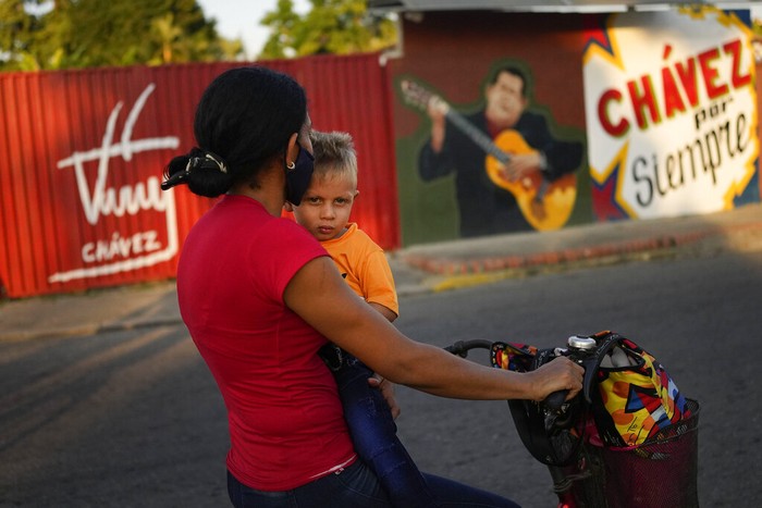 A boy pulls a suitcase on wheels as he walks past a mural of the late Venezuelan President Hugo Chavez in Chavez's hometown of Sabaneta, in Barinas state in Venezuela, Friday, Jan. 7, 2022. The country's highest court disqualified opposition candidate Freddy Superlano as he was leading the count in November's gubernatorial election in Barinas, apparently defeating Argenis Chavez, the brother of late President Hugo Chavez's, and ordered a re-run on Jan. 9. (AP Photo/Matias Delacroix)