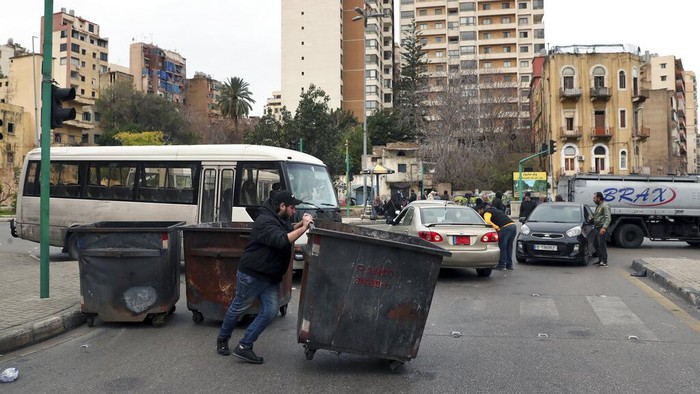 A man blocks a road with garbage containers during a general strike by public transport and labor unions paralyzed Lebanon to protest the country's deteriorating economic and financial conditions in Beirut, Lebanon, Thursday, Jan. 13, 2022. (AP Photo/Bilal Hussein)