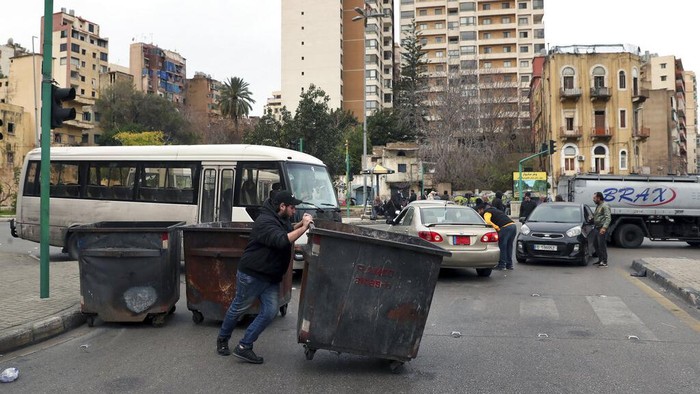 Protes Krisis Ekonomi, Pekerja di Lebanon Mogok hingga Blokir Jalan A man blocks a road with garbage containers during a general strike by public transport and labor unions paralyzed Lebanon to protest the country's deteriorating economic and financial conditions in Beirut, Lebanon, Thursday, Jan. 13, 2022. (AP Photo/Bilal Hussein)