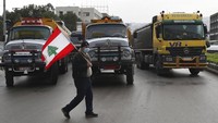 Seorang pengemudi truk memegang bendera Lebanon ketika pengemudi lain memblokir jalan raya utama dengan kendaraan mereka selama pemogokan. (AP/Bilal Hussein)