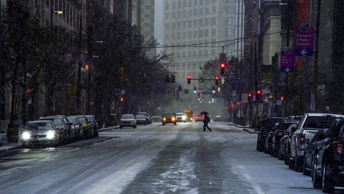 A pedestrian uses an umbrella as they cross Liberty Avenue, in downtown Pittsburgh, as snow begins to fall during a winter storm that will impact the region on Sunday night, Jan. 16, 2022. (Alexandra Wimley/Pittsburgh Post-Gazette via AP)