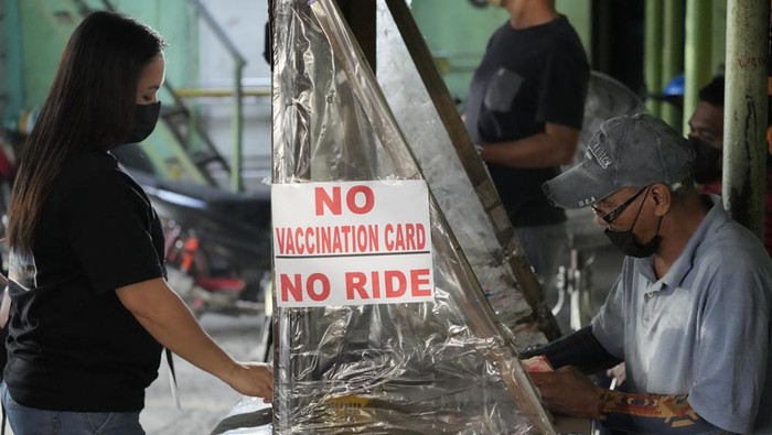 A woman stands beside a sign to remind passengers to show their vaccination card before riding at a jeepney terminal in Quezon city, Philippines on Monday, Jan. 17, 2022. People who are not fully vaccinated against COVID-19 were banned from riding public transport in the Philippine capital region Monday in a desperate move that has sparked protests from labor and human rights groups. (AP Photo/Aaron Favila)