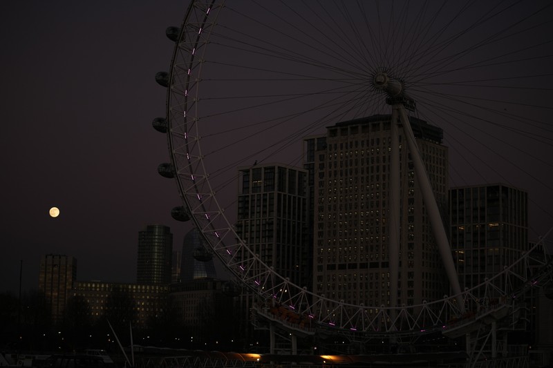 The first full moon of the year known as a Wolf Moon is seen behind different clock faces showing different times, with the correct time at right, as refurbishment work continues on the Elizabeth Tower, known as Big Ben, and the Houses of Parliament, in London, Monday, Jan. 17, 2022. (AP Photo/Matt Dunham)