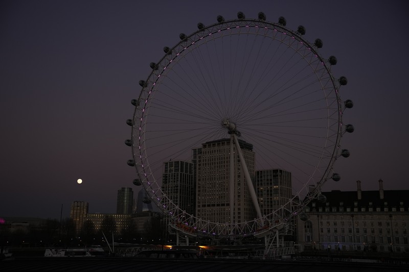 The first full moon of the year known as a Wolf Moon is seen behind different clock faces showing different times, with the correct time at right, as refurbishment work continues on the Elizabeth Tower, known as Big Ben, and the Houses of Parliament, in London, Monday, Jan. 17, 2022. (AP Photo/Matt Dunham)