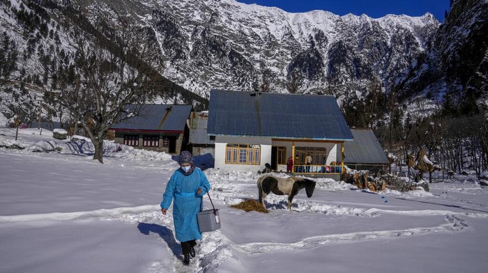Masrat Farid, a healthcare worker, carries vaccines as she walks on a snow covered field after administering doses to young girls during a COVID-19 vaccination drive in Gagangeer, northeast of Srinagar, Indian controlled Kashmir, Jan. 12, 2022. (AP Photo/Dar Yasin)