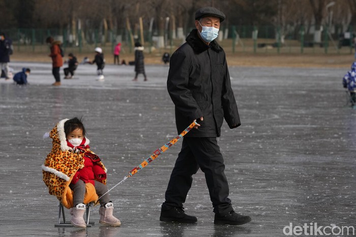 Residents play on a frozen pond surface near the iconic Bird's Nest Stadium in Beijing, China, Tuesday, Jan. 18, 2022. China has locked down parts of Beijing's Haidian district following the detection of three cases, just weeks before the capital is to host the Winter Olympic Games. (AP Photo/Ng Han Guan)