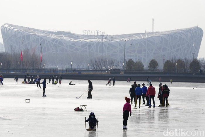 Bermain di Taman Kota yang Membeku Residents play on a frozen pond surface near the iconic Bird's Nest Stadium in Beijing, China, Tuesday, Jan. 18, 2022. China has locked down parts of Beijing's Haidian district following the detection of three cases, just weeks before the capital is to host the Winter Olympic Games. (AP Photo/Ng Han Guan)