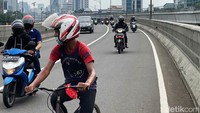 Dengan memakai helm motor, pesepeda itu melintas di flyover Pancoran yang lalu lintasnya ramai lancar.