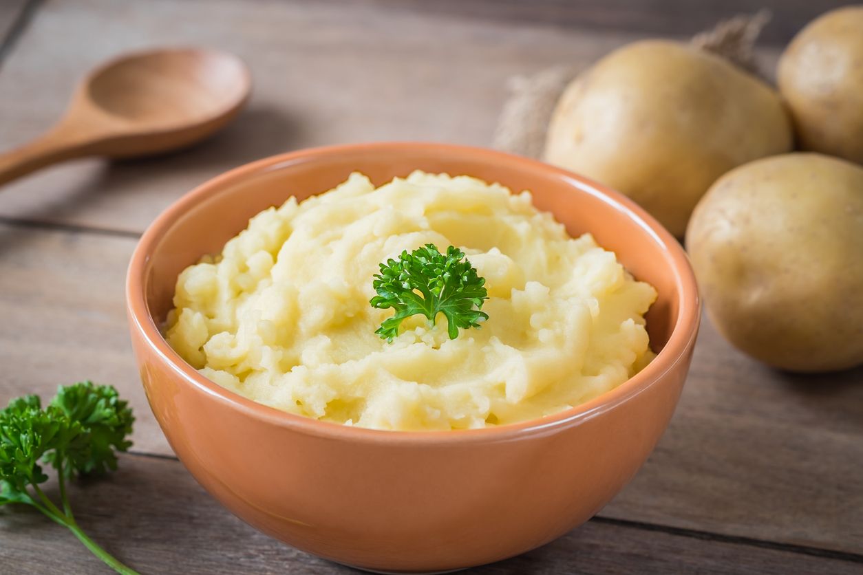 Mashed potato in bowl and fresh potatoes on wooden table