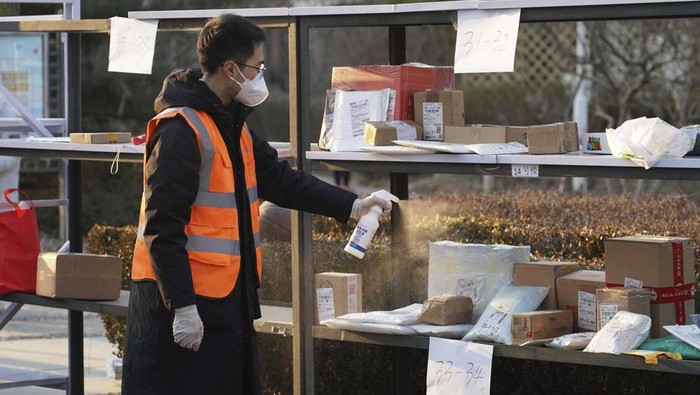 In this photo released by Xinhua News Agency, a staff member disinfects parcels at a community under close-off management where a locally transmitted COVID-19 case was found in Haidian in Beijing, China on Tuesday, Jan. 18, 2022. (Ren Chao/Xinhua via AP)