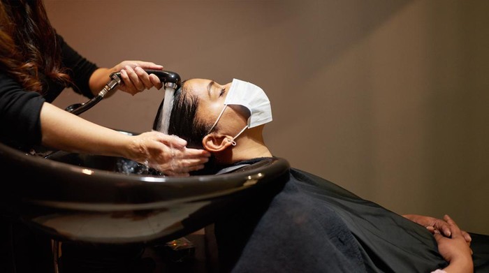 Young woman wearing a protective face mask getting her hair washed by a hairdresser in a salon