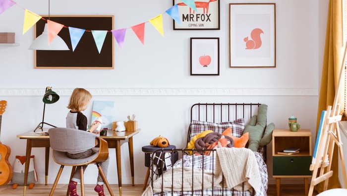 Cute little girl sitting at desk in her stylish vintage bedroom with workspace