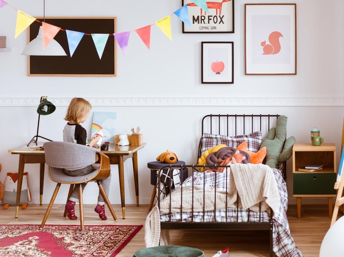 Cute little girl sitting at desk in her stylish vintage bedroom with workspace