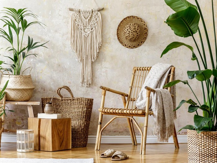 Stylish and floral composition of living room interior with rattan armchair, a lot of tropical plants in design pots, decoration and elegant personal accessories in cozy home decor. Wabi sabi concept.