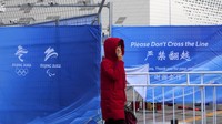 Seorang wanita menarik masker wajahnya untuk membantu melindungi dari virus corona saat dia berjalan di dekat area barikade di dekat Main Press Center (MPC) untuk Olimpiade Musim Dingin di Beijing. (AP/Andy Wong)