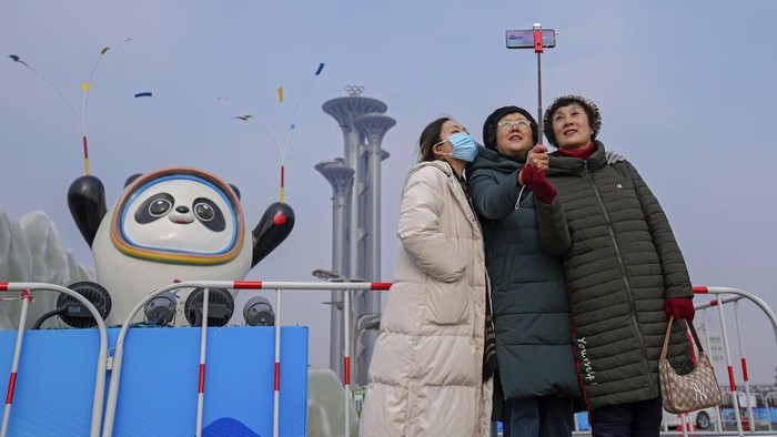 Olimpiade Musim Dingin Digelar Tertutup, Warga Beijing Kecewa A woman wearing a face mask to help protect from the coronavirus takes a selfie with her companion against a Beijing Winter Olympics Mascot and Olympic Tower in Beijing, Wednesday, Jan. 19, 2022. China has locked down parts of Beijing's Haidian district following the detection of three cases, just weeks before the capital is to host the Winter Olympic Games. (AP Photo/Andy Wong)