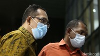 Itong tampak mengenakan kemeja batik, bermasker, dan membawa tas kecil.
