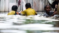 Anak-anak asyik bermain di tengah banjir.