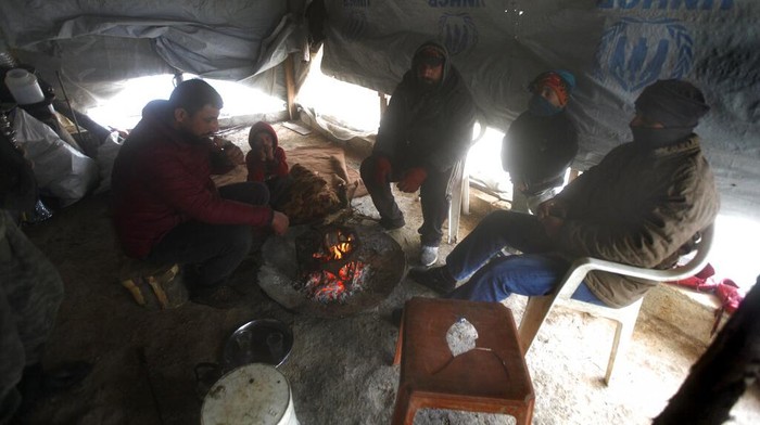 Warga di Lebanon Bertahan Hidup Kala Dihantam Badai Salju Displaced Syrians warm themselves around a fire inside a tent at a refugee camp near the southern port city of Zahrani, Lebanon, Wednesday, Jan. 19, 2022. A snowstorm in the Middle East has left many Lebanese and Syrians scrambling to find ways to survive. Some are burning old clothes, plastic and other hazardous materials to keep warm as temperatures plummet and poverty soars. (AP Photo/Mohammed Zaatari)