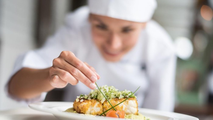 Cook decorating a plate and putting the ultimate touches - focus on foreground