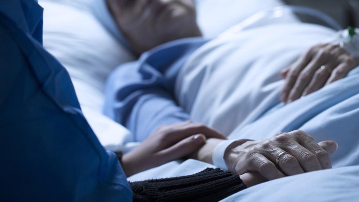 Young woman holding hands and saying goodbye to her dying of cancer mother in hospice