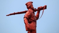 Patung berwarna merah tembaga, berseragam layaknya pelajar dengan menengteng buku di tangan kanan dan senjata laras panjang di pundak kirinya berdiri di antara Jalan Stasiun Timur dan Jalan Kebon Jukut, Kota Bandung.