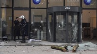 Polisi tampak berjaga di area gedung yang bagian pintu masuknya rusak akibat demo menolak vaksinasi COVID-19 yang berujung ricuh di Belgia, Minggu (23/1/2022) waktu setempat. AP Photo/Geert Vanden Wijngaert.