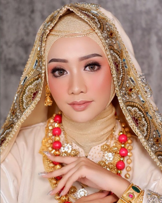 Tren Peach Glam Look dipadu dengan gaun pengantin adat membuat pengantin terlihat memesona. Tanpa mencukur bagian alis dan menggunakan airbrush makeup, MUA Tasyafaurikamakeup, menggunakan hijab glitter agar menambah kesan mewah dan glamour. Foto: Dok. Instagram @tasyafaurikamakeup.