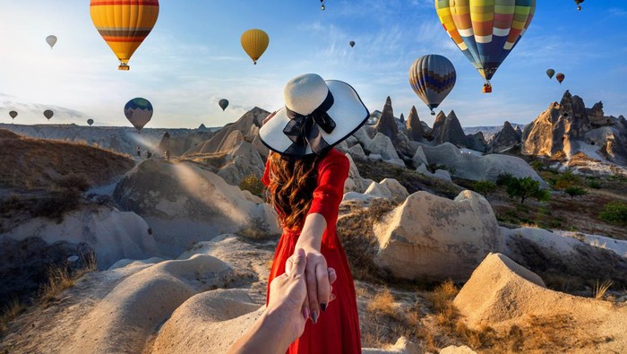 Women tourists holding mans hand and leading him to hot air balloons in Cappadocia, Turkey.