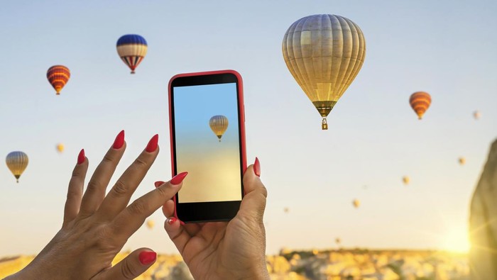 Smartphone in the hands of a woman  taking pictures of a beautiful landscape and balloons in Cappadocia. Sunrise time, dreamy travel concept