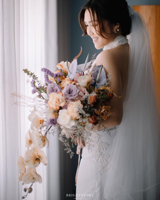 Sedangkan istrinya, Cindy Maria, memakai gaun pernikahan putih berkerah halter. Busana dari rancangan desainer Trifena Stephanie tersebut terlihat hadir dengan detail sulaman bunga yang cantik.Foto: Instagram @thebrightstory