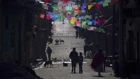 Warga berjalan di sepanjang jalan yang dihiasi dengan potongan kertas tisu berwarna yang disebut “papel picado, di komunitas Adat Puerpecha di Comachuen, Meksiko.
