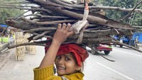 Anak tersenyum melihat kamera saat berjalan pulang dengan membawa kayu bakar di tengah udara dingin Prayagraj, India, (24/1/2022).  Sebagian besar wilayah utara India terus mengalami kondisi dingin di awal tahun. (Foto AP/Rajesh Kumar Singh)