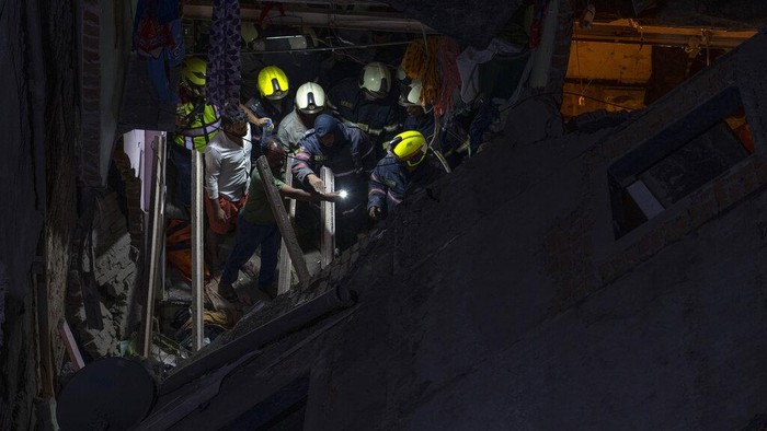 Fire brigade personnel along with others clear debris after a 5-story building collapsed at a slum in Mumbai, India, Wednesday, Jan. 26, 2022. (AP Photo/Rafiq Maqbool)