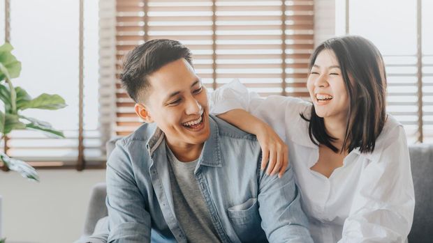 Happy Asian couple having fun and laughing together in living room at home