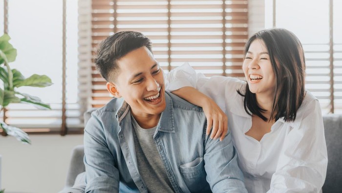 Happy Asian couple having fun and laughing together in living room at home