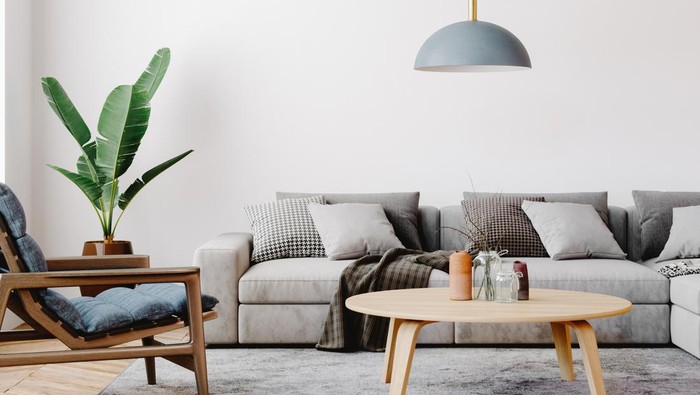 Modern living room setup with classic parquet floor. Furnished with light gray sofa, blue arm chair with wooden frame, modern blue ceiling lamp, wooden coffee table and gray carpet.