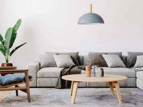 Modern living room setup with classic parquet floor. Furnished with light gray sofa, blue arm chair with wooden frame, modern blue ceiling lamp, wooden coffee table and gray carpet.