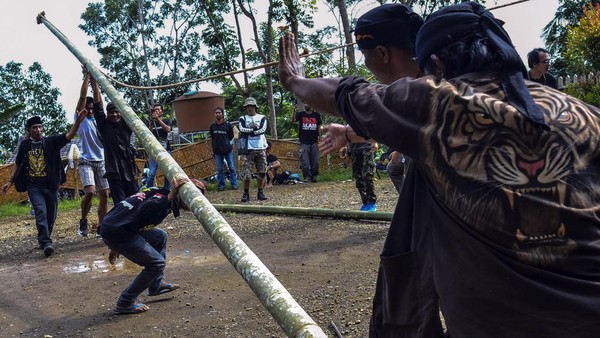 Tidak jauh dari lokasi keramaian, sejumlah pria berpakaian serba hitam bahu-membahu mendirikan dua batang bambu sepanjang 16 meter ke dalam dua lubang sedalam 60 meter.   