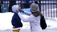 Seorang ibu membetulkan penghangat kepala anaknya di taman kota Pittsburgh, AS (20/1/2022). Bentuk perhatian kecil ini patut dibiasakan lagi. (Matt Freed/Pittsburgh Post-Gazette via AP)