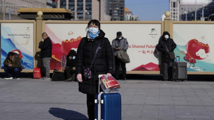 A traveler waits outside the Beijing railway station with her suitcase in Beijing, China, Friday, Jan. 28, 2022. The Beijing Winter Olympics is coinciding with the Chinese Lunar New Year and renewed Covid outbreaks prompting the Chinese authorities to call on the public to stay where they are instead of traveling to their hometowns for the years most important family holiday.