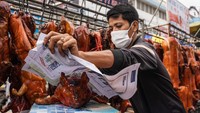 Seorang penjual membungkus babi panggang di pasar.