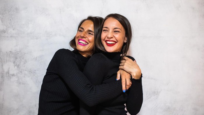 A portrait of two young women with different skin tones hugging and laughing