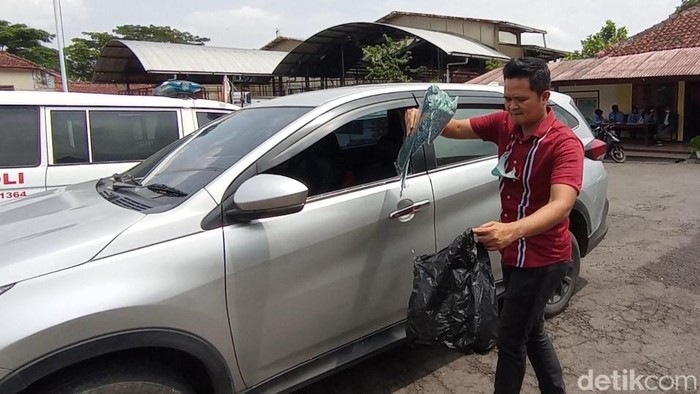Polisi membantu membereskan pecahan kaca mobil korban.