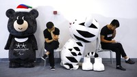 Para pekerja melihat ponsel mereka di sebelah maskot untuk Olimpiade Musim Dingin dan Paralimpiade Pyeongchang 2018 di dekat stan Korea Selatan selama Pameran Olahraga Musim Dingin Dunia di Beijing, (7/9/2017). (AP Photo/Andy Wong)