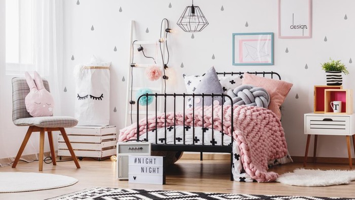Pink knit blanket on girls bed with pillows in colorful bedroom with ladder, chair and plant