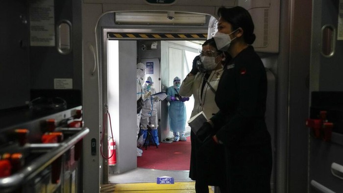 Melihat Kehidupan dalam 'Gelembung' di Olimpiade Beijing Airline crew are greeted by personnel dressed in protective gear as the plane arrives at the Beijing Capital International Airport ahead of the 2022 Winter Olympics, Jan. 30, 2022, in Beijing. (AP Photo/Kiichiro Sato)
